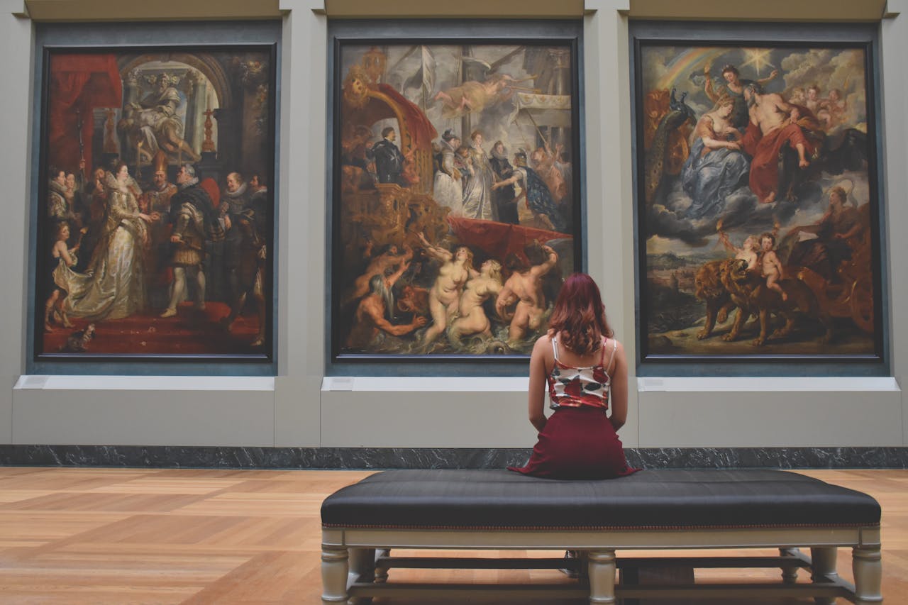 hero-img-01 A woman observes classic paintings in an elegant museum gallery.